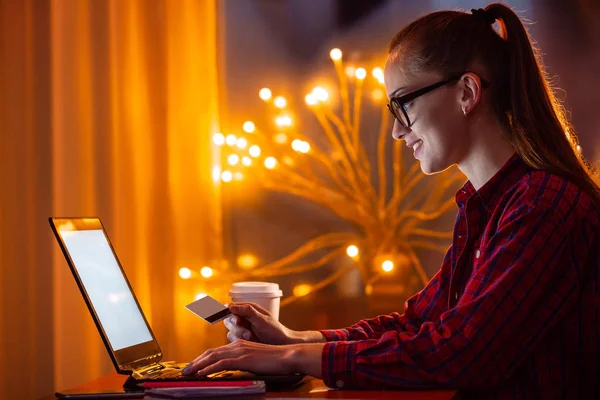 Joven, chica atractiva en gafas usando el ordenador portátil y la tarjeta de crédito f — Foto de Stock