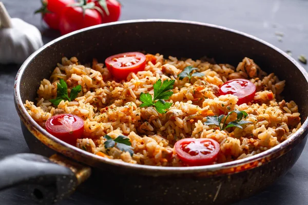 Koyu bir arka plan üzerinde öğle yemeği için bir tavada tavuk, taze maydanoz ve olgun sebze ile ev yapımı lezzetli pilav