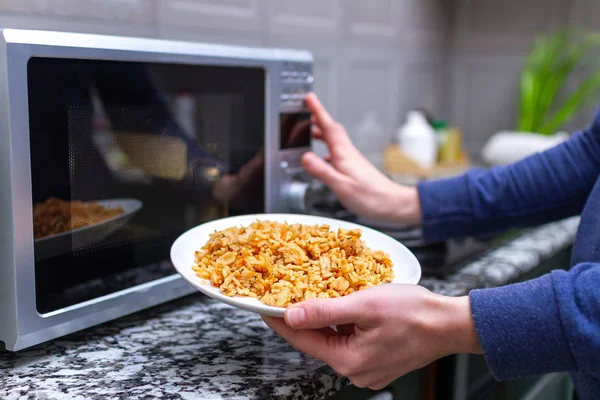 Verwendung einer Mikrowelle, um einen Teller hausgemachtes Pilaf zum Mittagessen zu erwärmen — Stockfoto