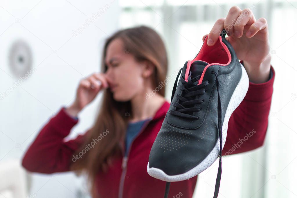 Woman is feeling unpleasant smell from sweaty running shoes afte