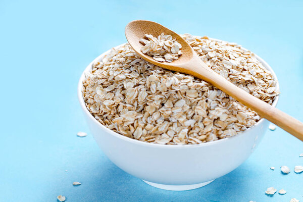 Сухая миска овсянки с деревянной ложкой на синем фоне. Овсяная хлопья
