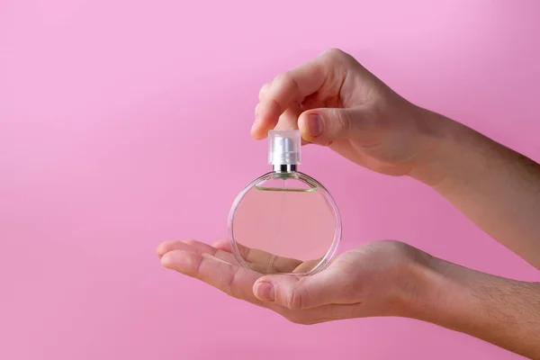 Bottle of women\'s perfume in hands on a pink background.