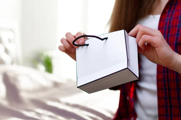 Mujer con camiseta sosteniendo una bolsa de regalo de papel en casa. Haciendo purcha —  Fotos de Stock