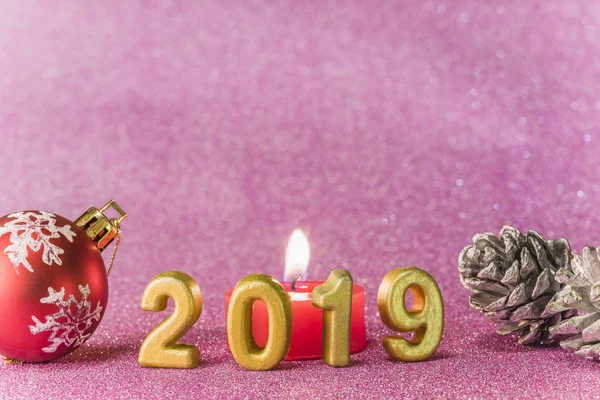 Pink glitter background for New Year\'s Cards with Christmas tree ball and silver bread apple around a candle and handmade golden numbers of 2019 year.