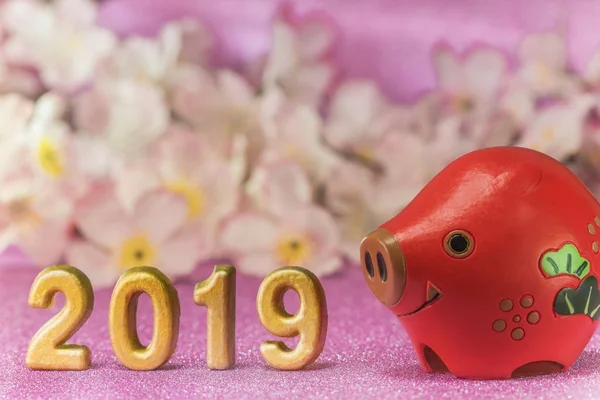 Pink glitter background with sakura cherry blossoms for japanese New Year's Cards with cute animal figurine of boar or pig and handmade golden numbers of 2019 year.