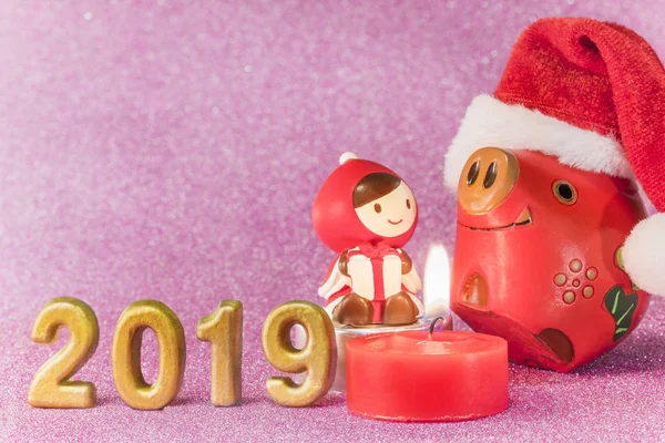 Pink glitter background for New Year\'s Cards with funny figurines of two boars  and chid with a Christmas hat dancing around a candle and handmade golden numbers of 2019 year.