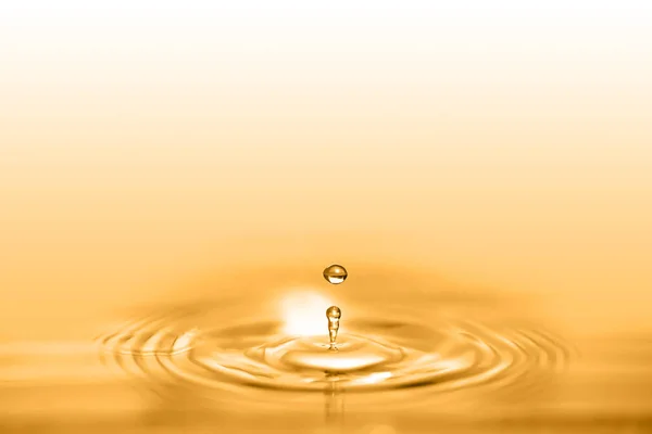 Closeup on drop of cosmetic golden oil liquid creating a circular wave.