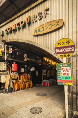 TOKYO, JAPAN - August 16 2018: Restaurant sign immitating an old retro bus stop sign on underpass Yurakucho Concourse wall under the railway line of the station Yurakucho. Japanese noodle stalls and sake bars revive the nostalgic years of Showa era. clipart