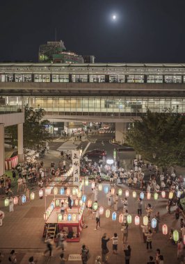 Tokyo, Japonya : 23 Ağustos 2018: Obon festivali için dekore edilmiş Nippori tren istasyonunun önündeki meydanın manzarası, geleneksel kostümlü bir kızın yaz gecesi taiko davul çaldığı kağıt fenerlerle aydınlatılmış bir yagura kulesiyle süslenmiştir..