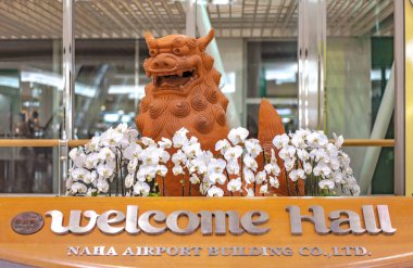 Okinawa Adası 'nın güneyindeki Naha Havalimanı' nın karşılama salonunda beyaz orkidelerle süslenmiş Japon Okinawa aslanı Shisa heykeli..