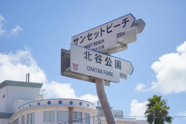Okinawa, Japonya - 18 Eylül 2018: Distorsiyon Seaside, Oak Fashion ve Depot Island Seaside'ın bulunduğu Okinawa adasındaki Chatan City'nin Amerikan köyünün alışveriş merkezinde Sunset Beach ve Chatan Park yazılı metal tabela