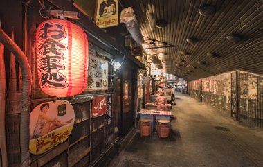 Tokyo, Japan - August 25,2019: Night view of the Yuraku Concourse underpass under the railway line of the station Yurakucho. Japanese noodle stalls and sake bars revive the nostalgic years of Showa air with old posters glued to the tunnel. clipart