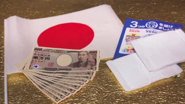 Maschere di stoffa, volantino e 100000 yen in contanti per COVID-19 su bandiera giapponese e carta dorata . — Video Stock