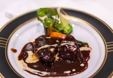 Biftek güveci ile ana Fransız ana yemeği kırmızı şarap sosunda kaynatılmış kırmızı şarap sosu ile altın kenarlı beyaz ve siyah bir yemek tabağında havuç gibi sebzeler.