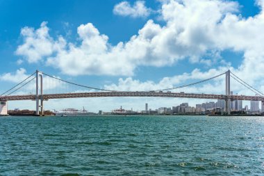 Tokyo Körfezi 'nde çift katmanlı asma Gökkuşağı Köprüsü. Arka planda Tokyo Limanı Uluslararası Konteyner Terminali' nin vinçleri var..