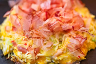 Okonomiyaki Japon omletine yakın plan. Bu da senin istediğin gibi pişmiş, doğranmış lahana ile hazırlanmış ve fırında pişirilmiş Katsuobushi adında kurutulmuş bonito parçacıkları ile kaplanmış demek..