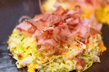 Okonomiyaki Japon omletine yakın plan. Bu da senin istediğin gibi pişmiş, doğranmış lahana ile hazırlanmış ve fırında pişirilmiş Katsuobushi adında kurutulmuş bonito parçacıkları ile kaplanmış demek..