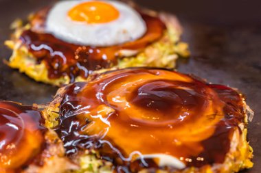 Kızarmış yumurta ve parçalanmış lahana ile hazırlanmış okonomiyaki Japon omleti, iki tarafı da sıcak bir tabakta pişmiş ve istiridye ve Worcestershire sosuyla çevrelenmiş..