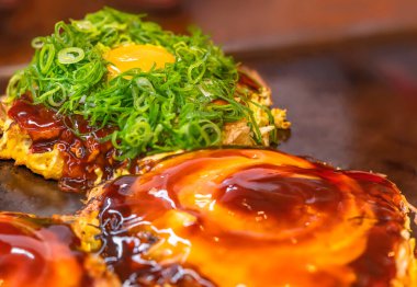 Okonomiyaki Japon omletinin üzerinde büyük miktarda doğranmış soğanla kaplanmış, sıcak tabakta pişirilmiş ve istiridye sosu ve Worcestershire sosuyla çevrelenmiş bir yumurta.