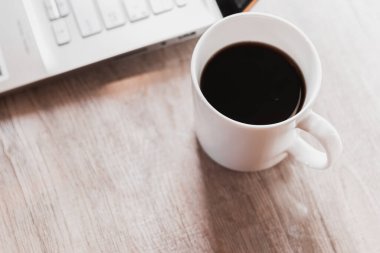 Siyah kahveyi beyaz fincanda, laptopu da ahşap masada kapat. Ev kavramından çalış