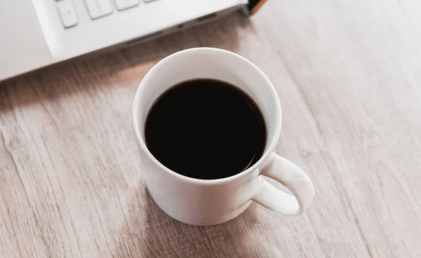 Siyah kahveyi beyaz fincanda, laptopu da ahşap masada kapat. Ev kavramından çalış