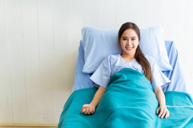 Asyalı genç bayan hastalar mavi gömlekler giyip parlak yüzlü yatakta yatıyorlar. Doktorun kontrol etmesini beklerken daha iyi semptomlar gösteriyorlar.