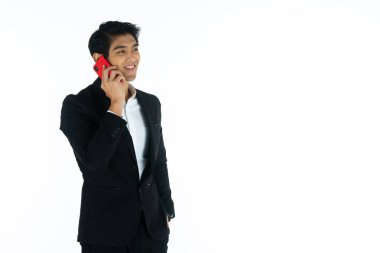 Yakışıklı genç işadamı Asya beyaz siyah saçlı siyah bir takım elbise giymek, bir gülümseme ve ayakta akıllı pozlar olmak. Akıllı telefonu tutun ve kullanın. Beyaz arka planda.
