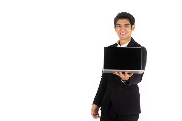 Yakışıklı genç işadamı Asya beyaz siyah saçlı siyah bir takım elbise giymek, bir gülümseme ve ayakta akıllı pozlar olmak. Bir bilgisayar dizüstü bilgisayarı tutun ve gösterin. Beyaz arka planda.