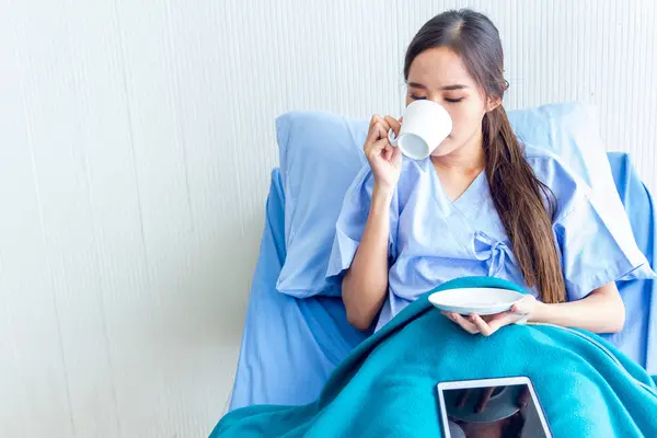 Pacientes asiáticas jóvenes están bebiendo agua tibia en una cama de paciente en la sala de recuperación. Y expresiones faciales brillantes en la sala del paciente . —  Fotos de Stock