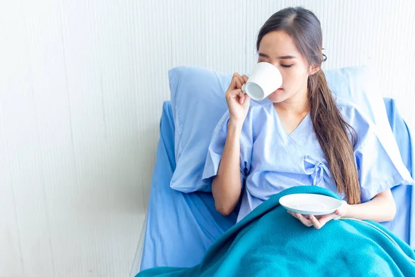Pacientes asiáticas jóvenes están bebiendo agua tibia en una cama de paciente en la sala de recuperación. Y expresiones faciales brillantes en la sala del paciente . —  Fotos de Stock