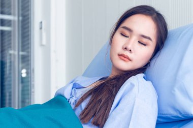 Yatakta yatan mavi gömlek giyen Asyalı genç kadın hastalar