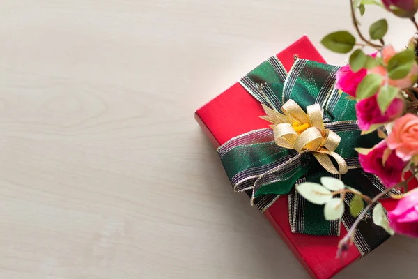 Red gift box with dark green ribbon and flowers placed on a tabl