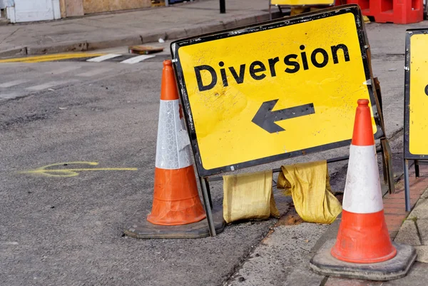 Yellow diversion sign and two road cones in a UK city street