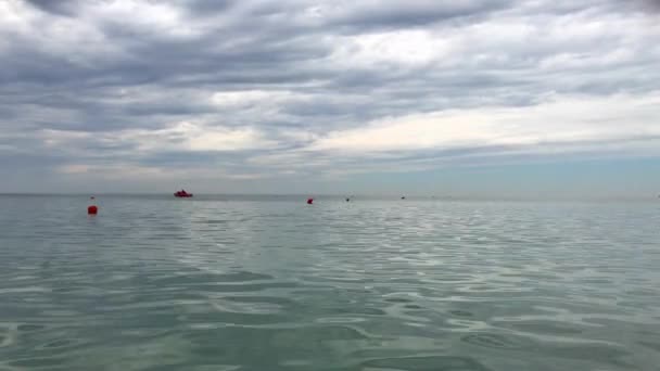 赤ブイ フロートと赤い救命艇は 雲の穴の低い灰色の雲の下の距離で穏やかなアクアマリン色の海の水に浮いたまま — ストック動画
