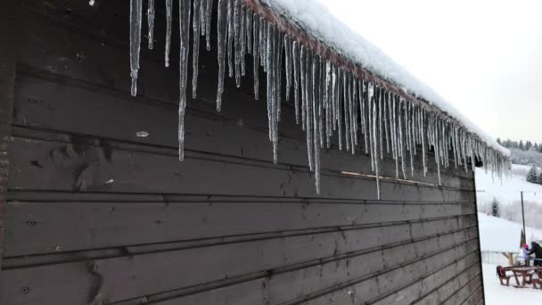 冬季滑雪胜地屋顶上的冰柱上滴滴水 背景滑雪者 冬季运动训练综合体附近木屋顶檐绳的冰柱 — 图库视频影像