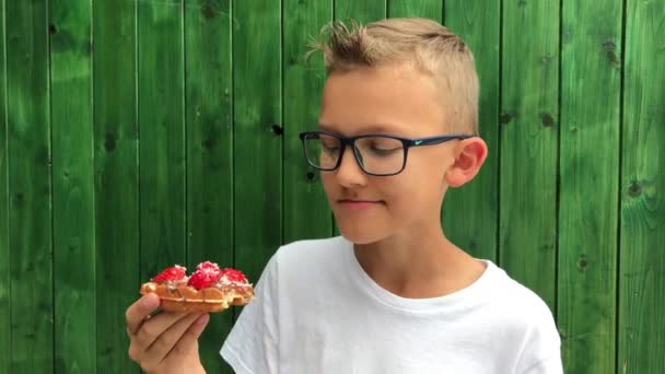 Brno, Česká republika - 09/15/2018: jídlo a pití Festival. Teenager chutnají vafle s jahodovou a sladkosti. Pár záběrů z mladík s brýlemi s chutné rychlé jídlo, žvýkání a usmíval se, zelené pozadí