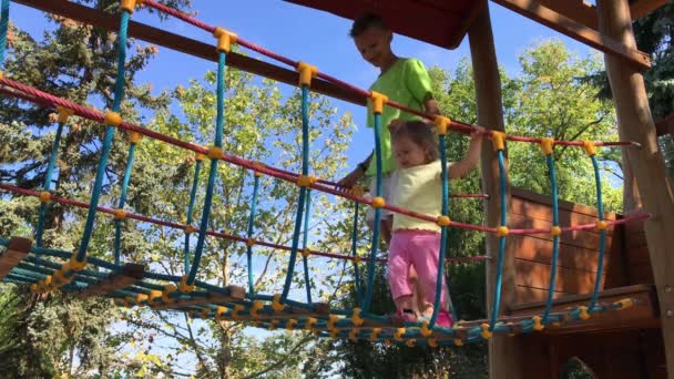 Dos Clips Niños Cruzan Puente Cuerda Suspendida Patio Recreo Día — Vídeos de Stock