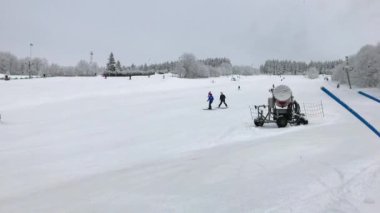 Kayak hocası genç kayakçı yokuş aşağı kayak kış gününde üzerinde durur. Kayak merkezinde kar canon yakınındaki yamaçta Kayak eğitim. İnsanlar kayak izinde. Pist üzerinde aşağı sürme öğrenme kayakçı kış sporu