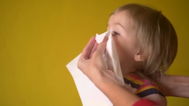 母はナプキン屋内での鼻の一撃 プロファイルに表示する小さな女の子を助けます 女性は幼児が彼女の鼻を吹いている間彼女の娘の顔の近くのナプキンを保ちます 大人が病気中に赤ちゃんを世話することを助ける — ストック動画