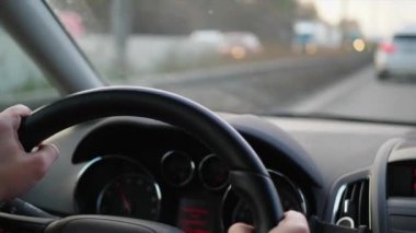 Onu ve araba sürüş sırasında otomobil dashboard ellerle direksiyon simidi Close-up. Taşıma sürücü karayolu üzerinde. Tekerlek, bakıcısı görünümü içinde araba odaklanmak. Etkin yolda odaklanmamış ulaşım öndeki pencere gördüm