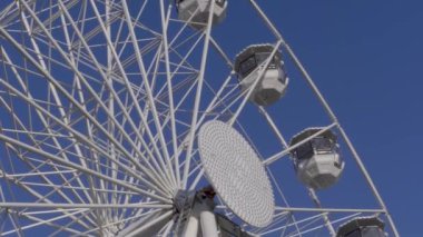 Dönme dolap üzerinde beyaz bulutlar ile mavi gökyüzü panayır üzerinde döner, yakın çekim. Güneşli bir gün, tanınmayan insanlarla gözlem tekerleği. Alt görünümü eğlence binmek. Karnaval binmek üzerinde panoramik çıkrık