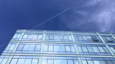 İş windows bina mavi gökyüzü ve beyaz bulutlar yansıtan ve uçak uçan iz buharı. Modern mimari güzel hava. Camlar güneş ışığı üzerinde şehirde. Parlak gün ofiste. Yansıma ayna desen İnşaat