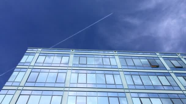 青い空と白い雲を反映し 飛行機を残して飛んで蒸気トレイルを Windows の構築ビジネス 天気の良い日の近代建築 市では太陽の光で染められた窓 明るい日のオフィス 建設のパターンが鏡に反射 — ストック動画