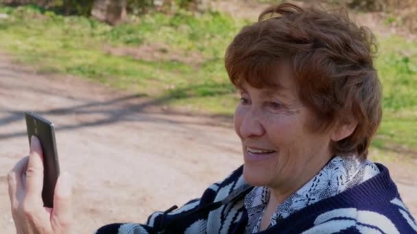 Starsza Kobieta Siedzi Smartfonem Zewnątrz Rozmowy Wideo Przez Telefon Komórkowy — Wideo stockowe