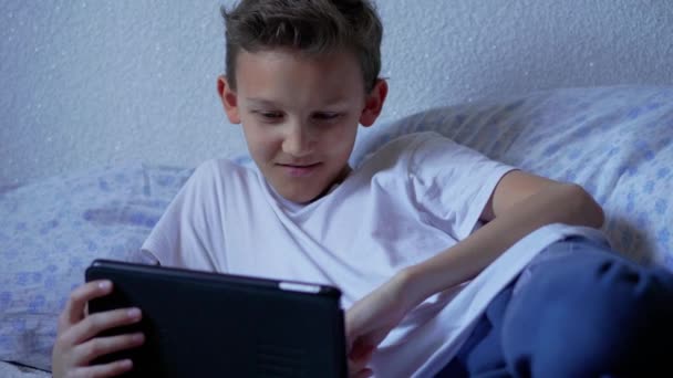 ティーンエイジャーの少年は 自宅でタブレット上の通話メッセンジャーを介して呼び出し ライブビデオをストリーミング スクリーナーの子供が話し 物語を記録します 寝室のパッド上のソーシャルネットワークを介しておしゃべりティーン ベッドでインターネットを使用する子供 モバイルデバイス上 — ストック動画