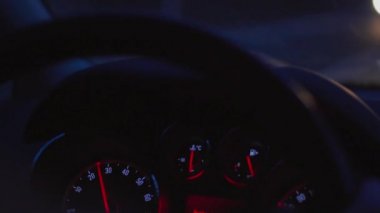 Otomobil panosu, hız göstergesi ile kontrol paneli, karanlıkta araba sürüş sırasında yakıt tüketimi, yakın. Göstergelere odaklanın, otomobilin içindeki bakıcı görünümüne. Yaklaşan trafiğin ışıkları. Geceleri direksiyonda odaklanmamış eller