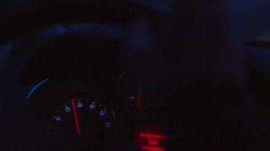 Araba sürüş otomobil panosu, karanlıkta sürme sırasında kontrol paneli. Sürücü elini tutan direksiyon simidi hız göstergesi, yakıt tüketimi, yakın çekim. Göstergelere odaklanın, otomobilin içindeki bakıcı görünümüne. Geceleri direksiyonda odaklanmamış eller