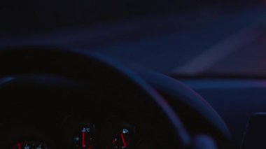 Araba sürüş otomobil panosu, karanlıkta sürme sırasında kontrol paneli, yaklaşan trafik ışıkları. Sürücü elini tutan direksiyon simidi hız göstergesi, yakıt tüketimi, yakın çekim. Göstergelere odaklanın, otomobilin içindeki bakıcı görünümüne. Odaklanmamış el