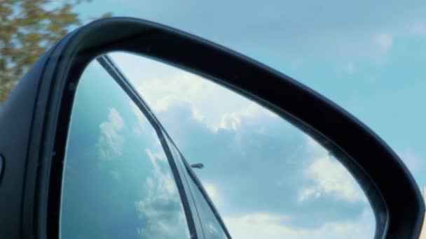 高速道路を走行中に青空と白い雲が反射する自動車右側のリアビューミラー 週末のコンセプト 車内のシッターまたは乗客の視点 黒いリアミラーへの眺め — ストック動画