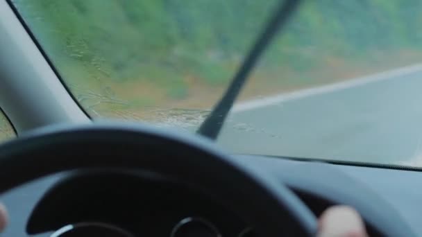 運転中に車のフロントウィンドウに雨が降り 雨を感知ワイパーを動かし クローズアップします フロントスクリーンの濡れた道路での輸送ドライブ 雨の日に手で焦点を合わせていないダッシュボード コントロールパネル ステアリングホイール 雨が飛び散るガラスに焦点を当てる — ストック動画